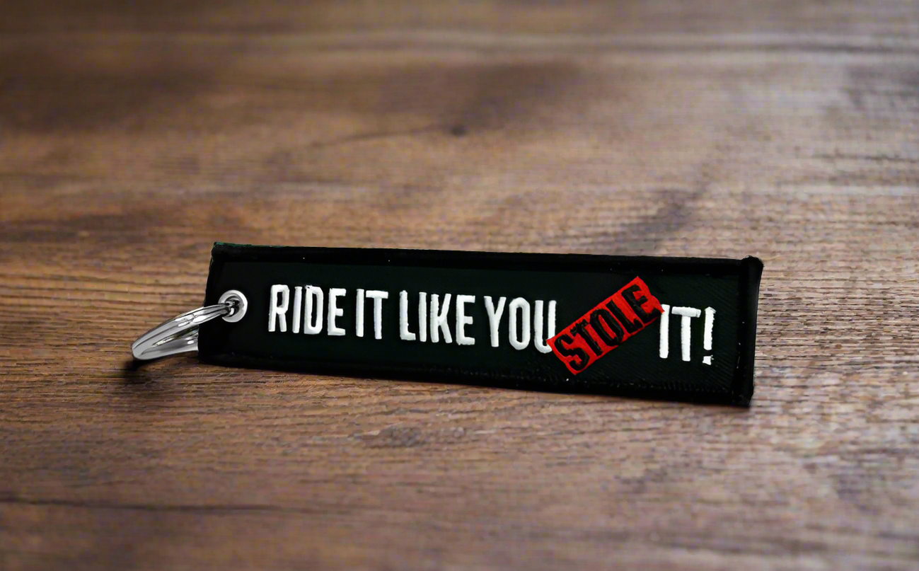 Black keychain with RIDE IT LIKE YOU STOLE IT text on a wooden surface.