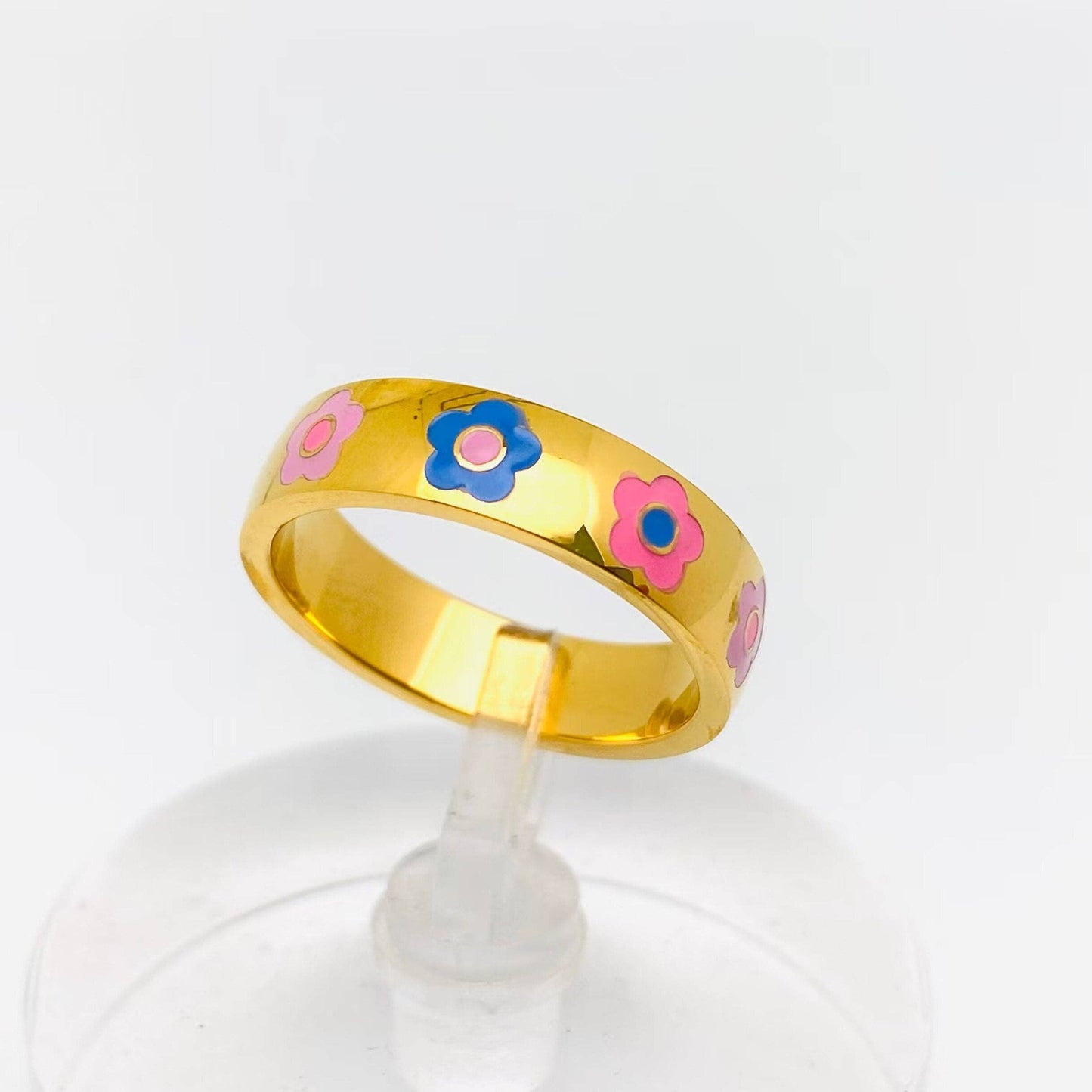 Gold ring with colorful flower designs on a clear stand.