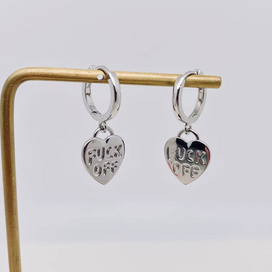 Silver heart-shaped earrings with FUCK OFF engraved, displayed on a gold stand.