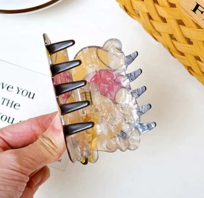 Clear floral hair claw clip with black claws, held over a notebook.