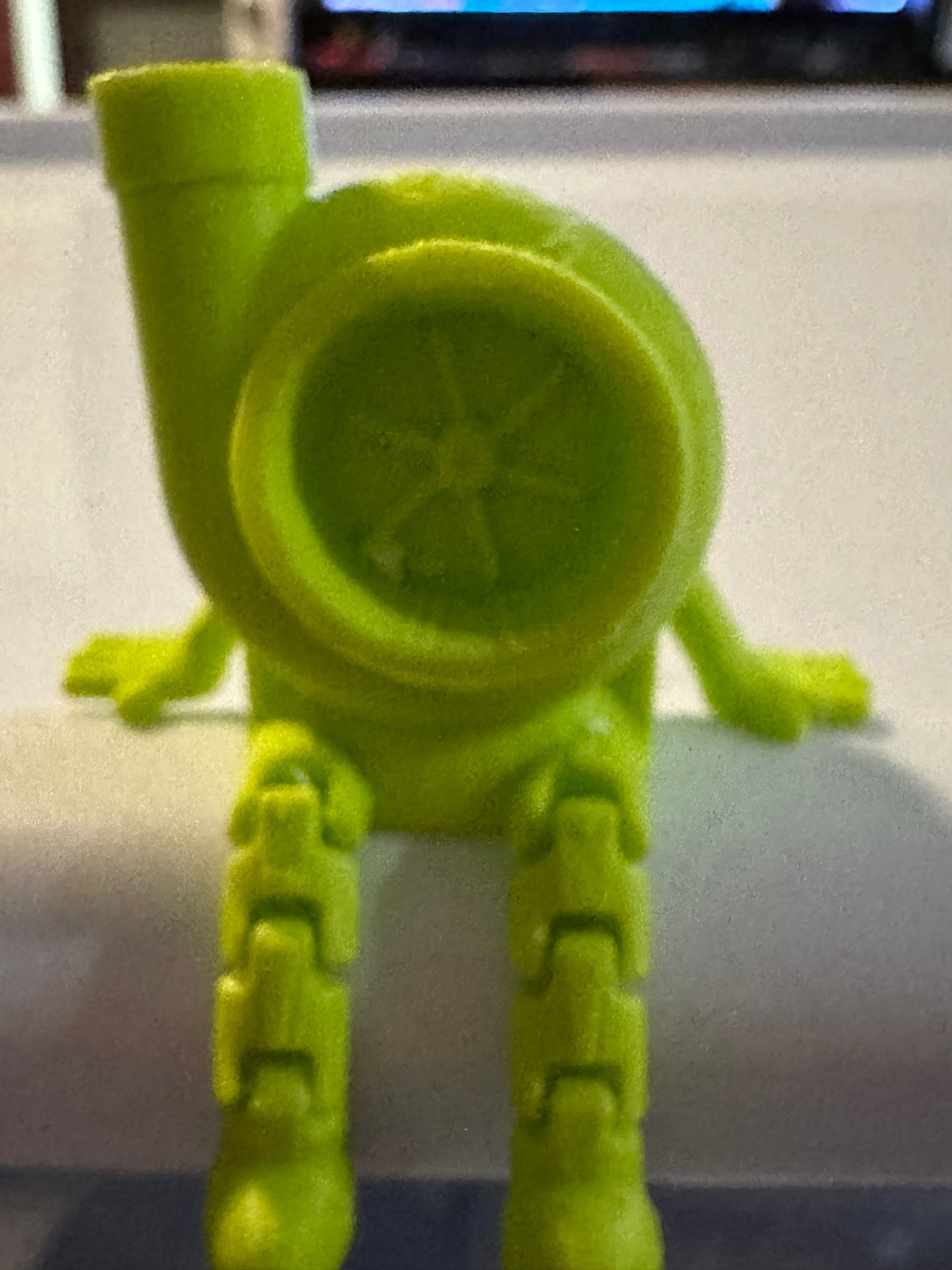 Green toy figure with a circular head and articulated limbs.
