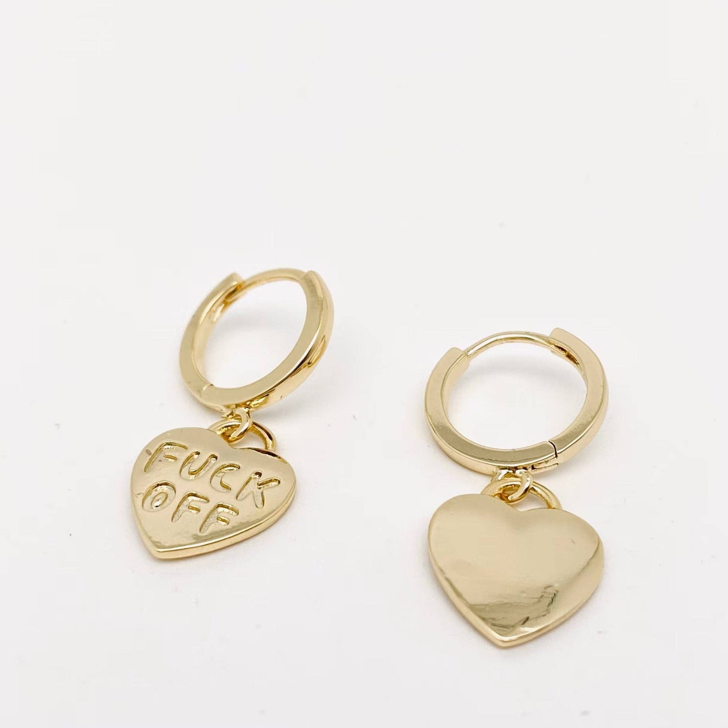 Gold hoop earrings with heart pendants, one engraved FUCK OFF.