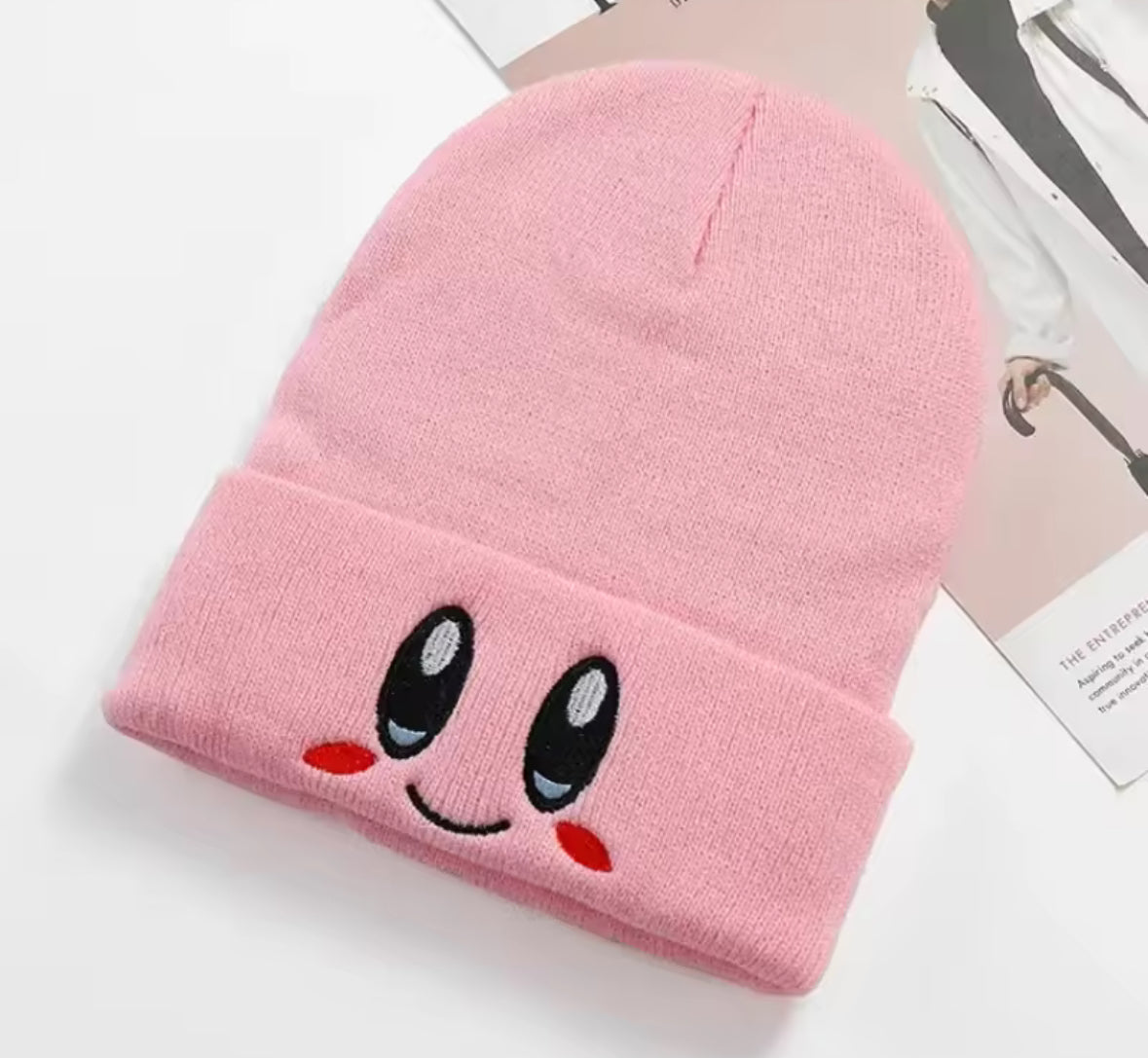 Pink knit beanie with cute face design featuring eyes and a smile.