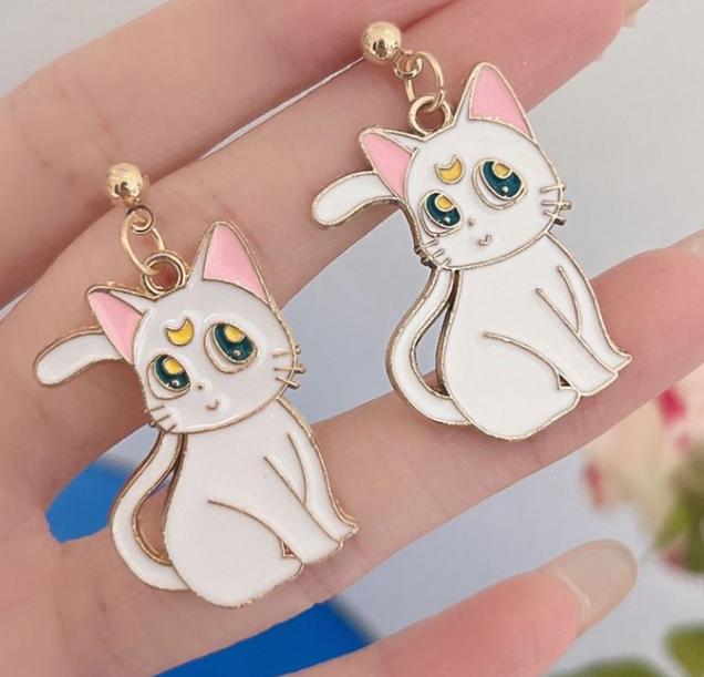 White cat earrings with yellow eyes and pink ears on hand.