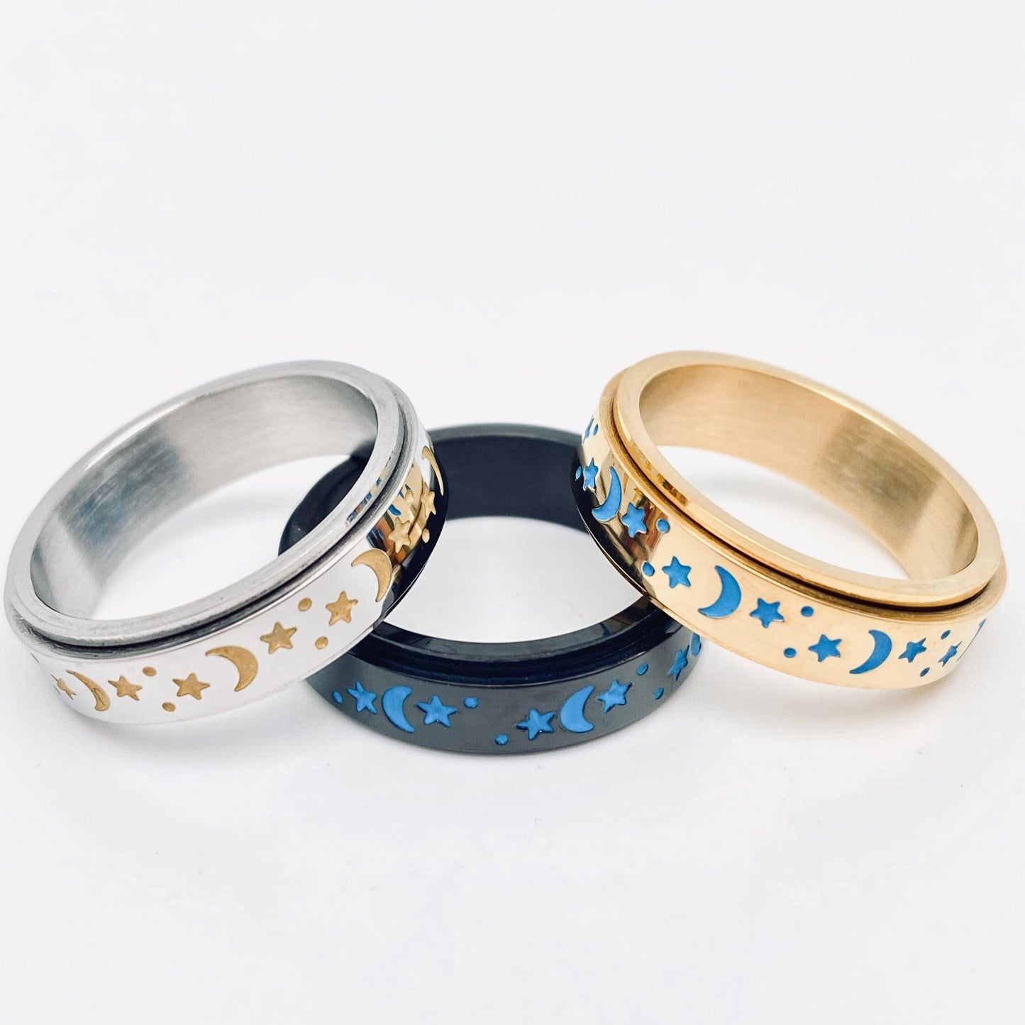 Three spinner rings with moon and star designs in silver, gold, and black.