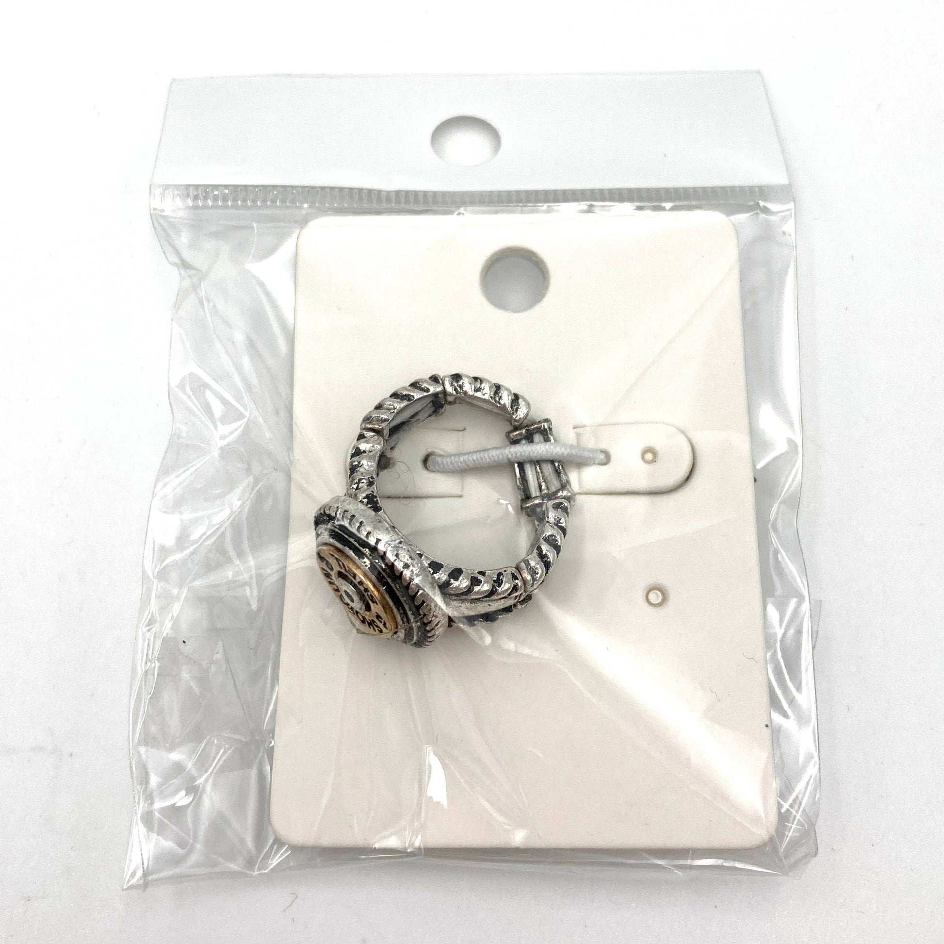 Silver ring with intricate design and central gear-like element in packaging.