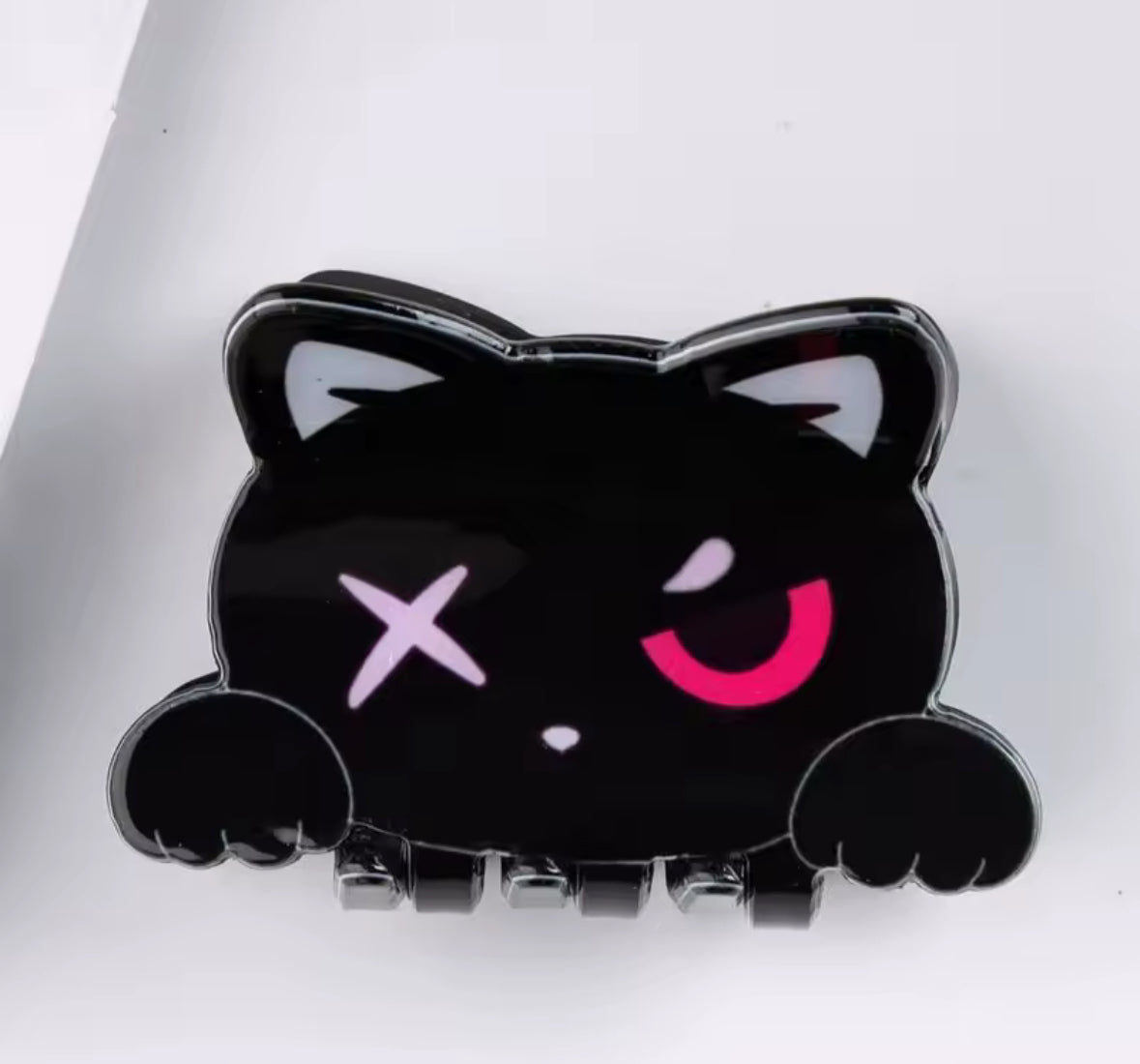 Black cat-shaped hair clip with pink eye and X mark on forehead.