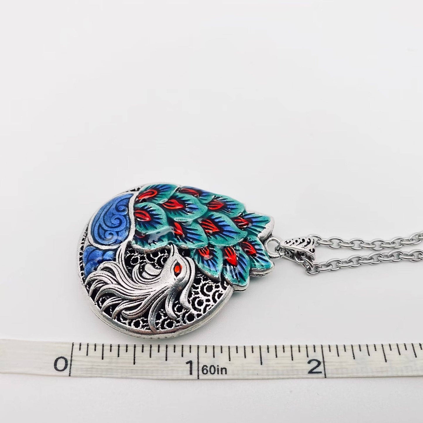 Colorful peacock feather pendant necklace with silver chain and ruler for scale.