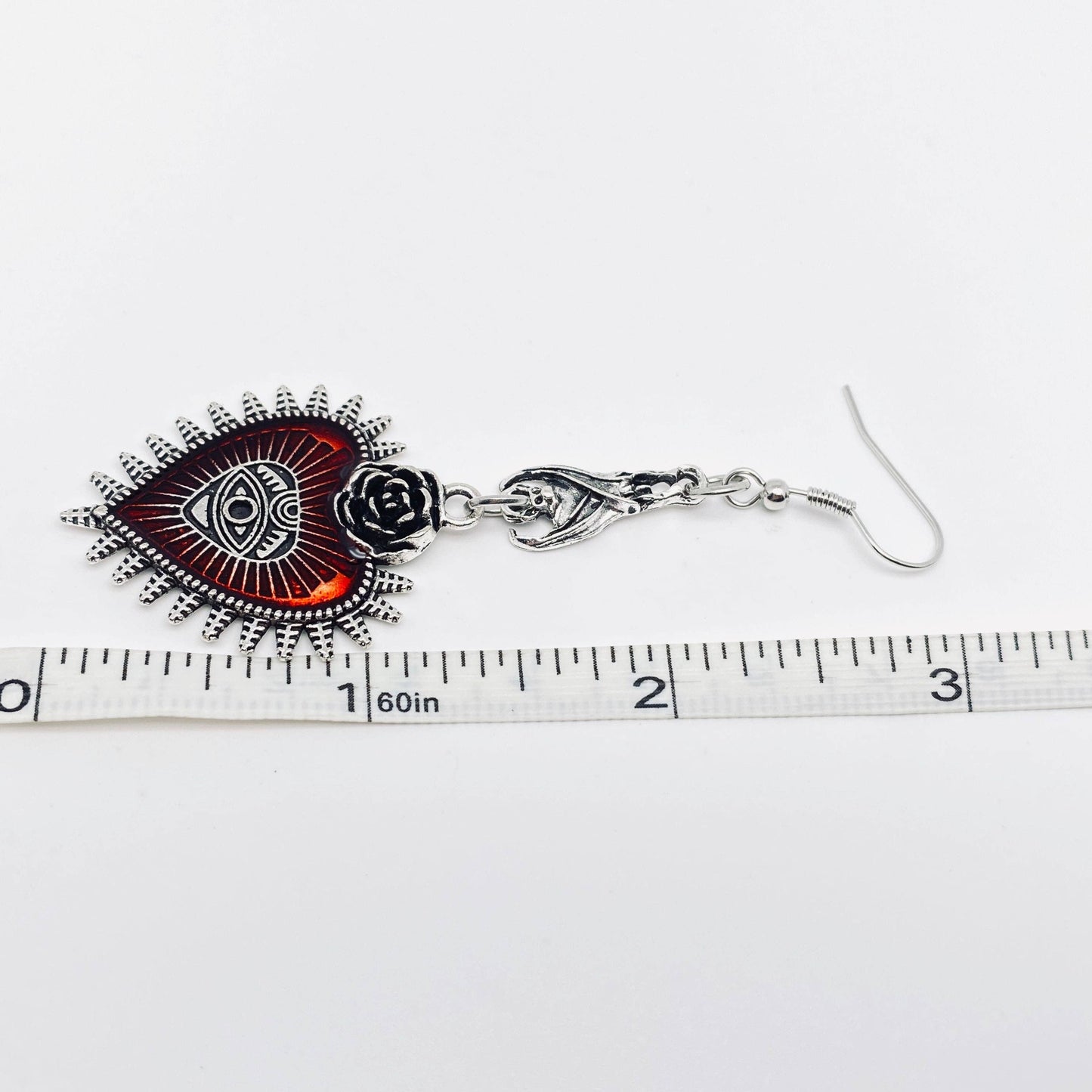 Silver eye and rose dangle earrings with ruler for size reference.