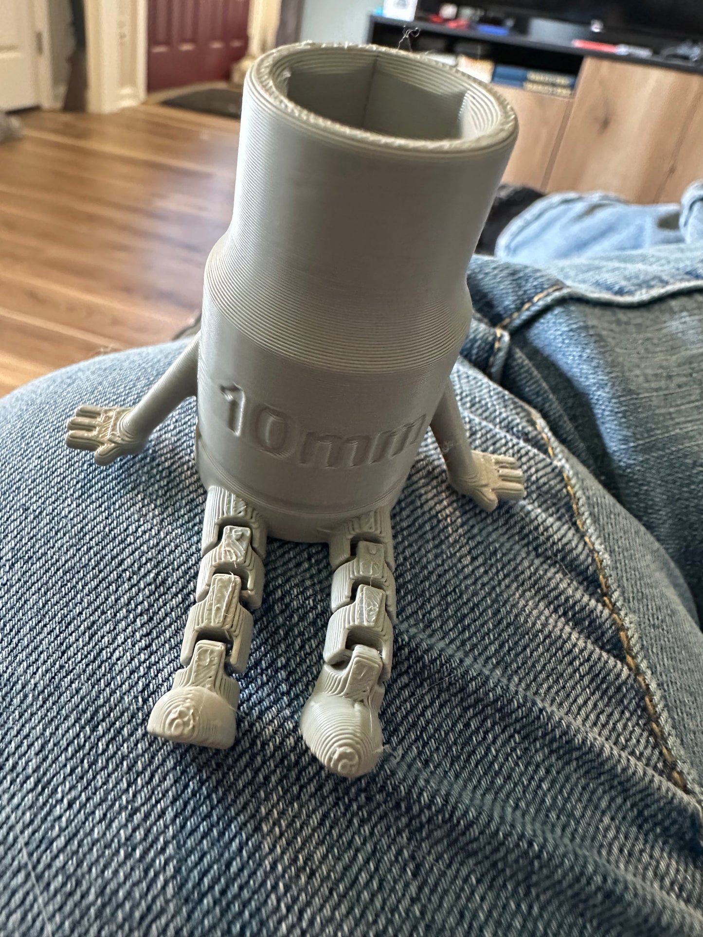 3D-printed robot figure with 10mm text, sitting on jeans.