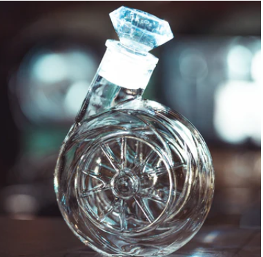 Clear glass bottle with wheel design and diamond-shaped stopper.