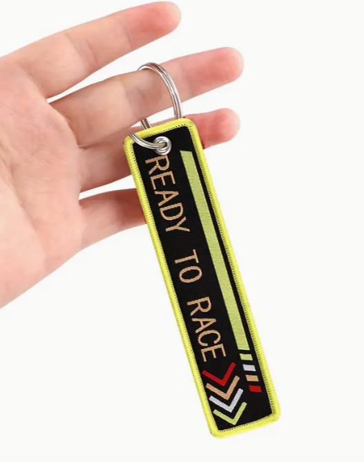 Hand holding READY TO RACE keychain with neon yellow border.