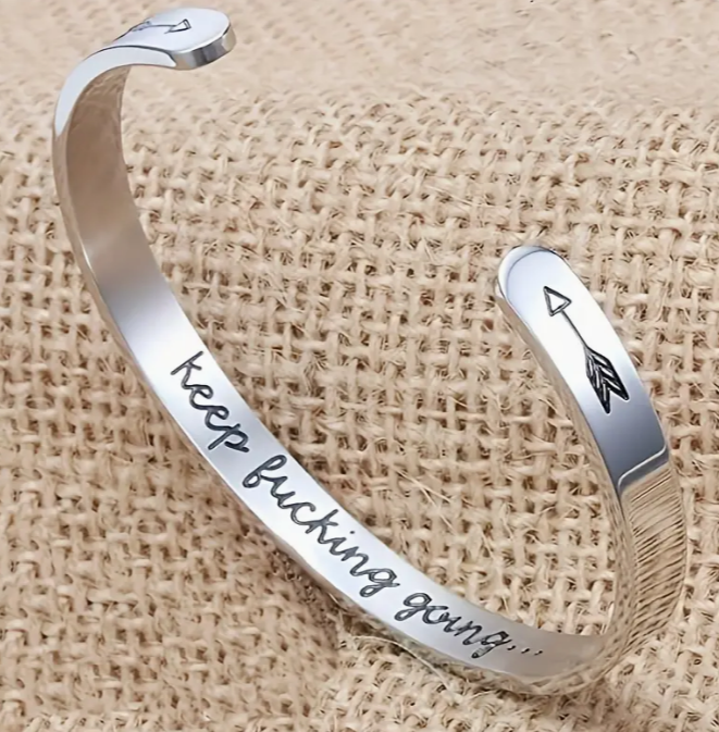 Silver cuff bracelet with keep fucking going... engraved on it.