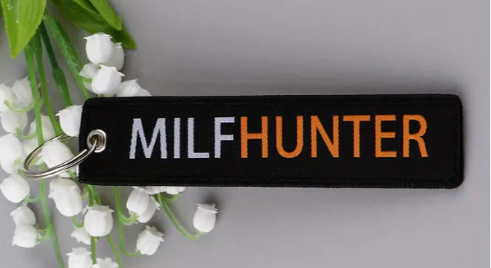 Black keychain with MILFHUNTER text in white and orange, surrounded by white flowers.