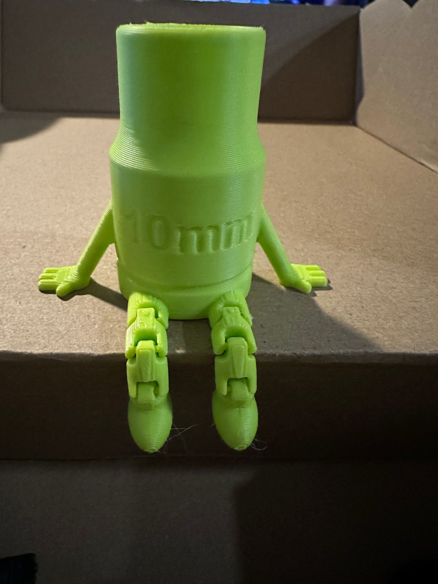 Green 3D-printed toy figure with 10mm text, sitting on a box.
