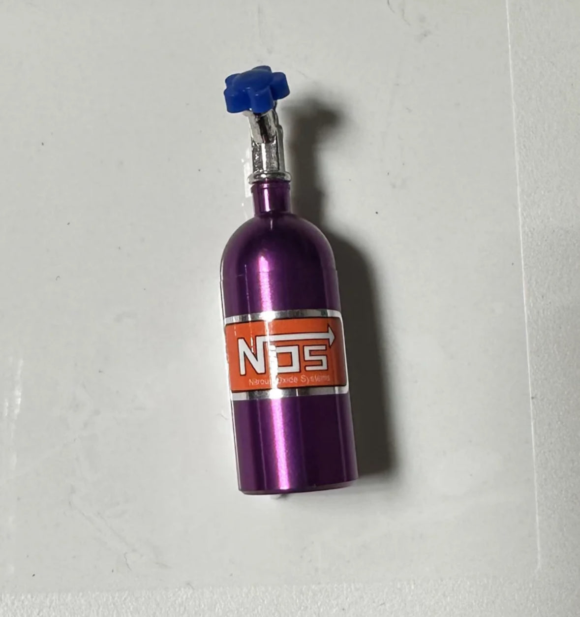 Purple NOS nitrous oxide bottle with blue cap on white surface.
