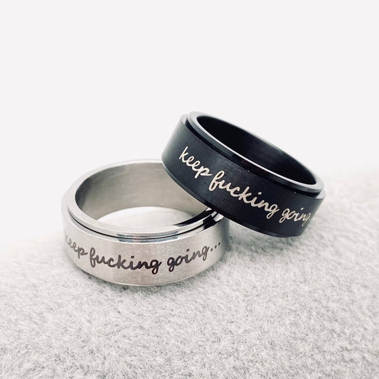 Two engraved rings with keep fucking going text, one silver and one black.