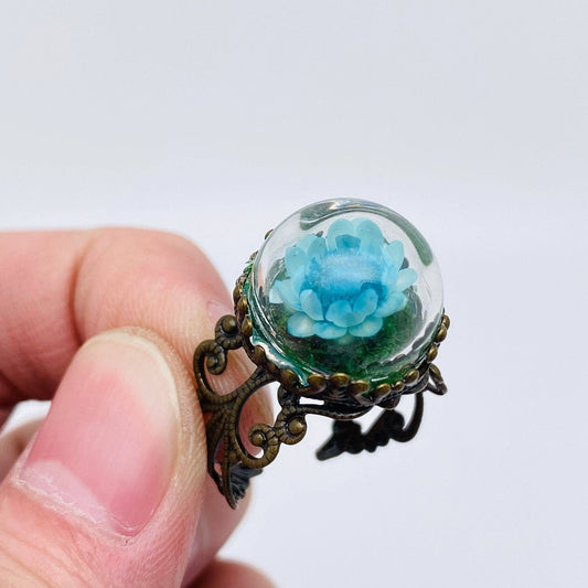 Blue flower in glass dome on ornate bronze ring.