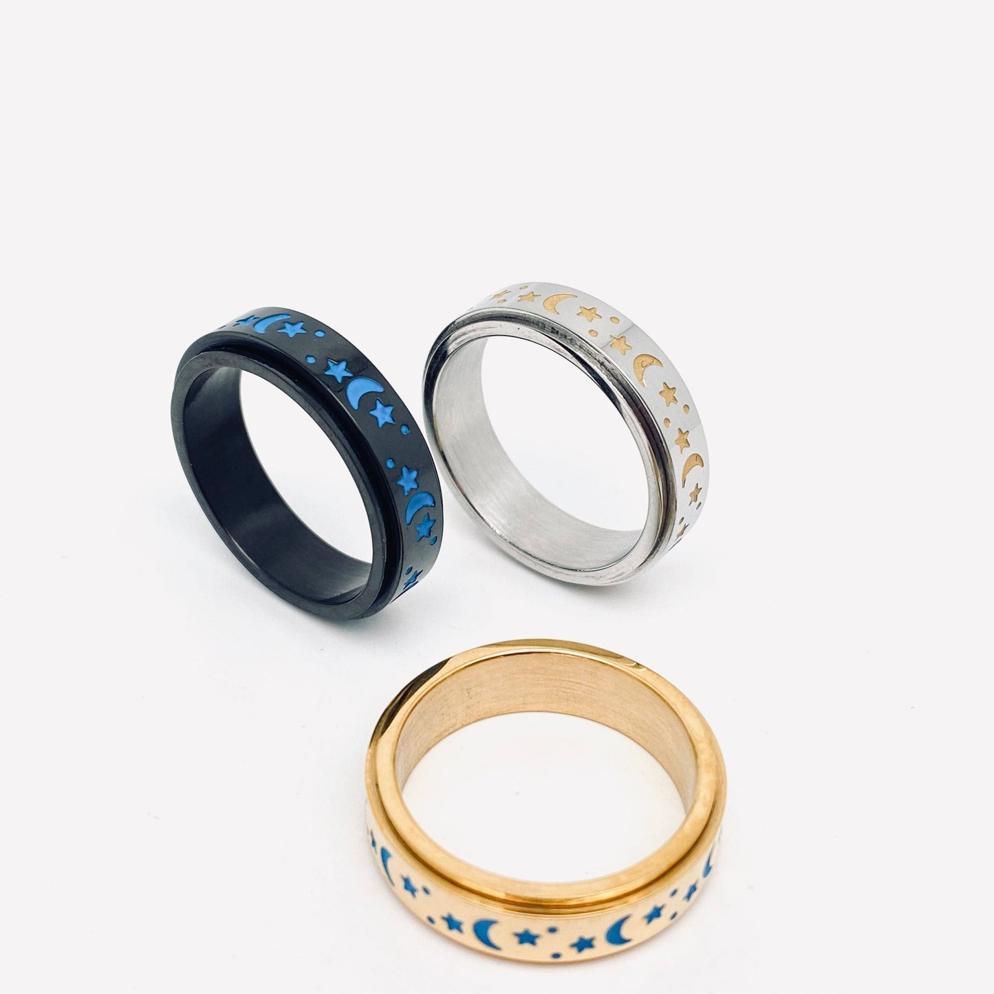 Three metallic rings with moon and star designs, black, silver, and gold.