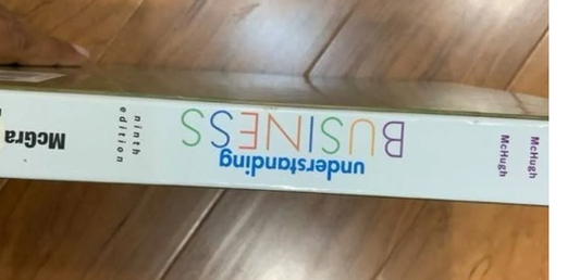 Cover of Understanding Business ninth edition book on wooden surface.