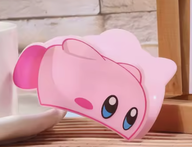 Pink Kirby plush toy with large eyes on wooden surface.