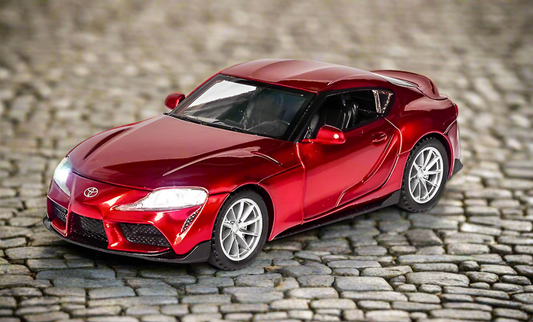 Red Toyota sports car model on cobblestone surface.