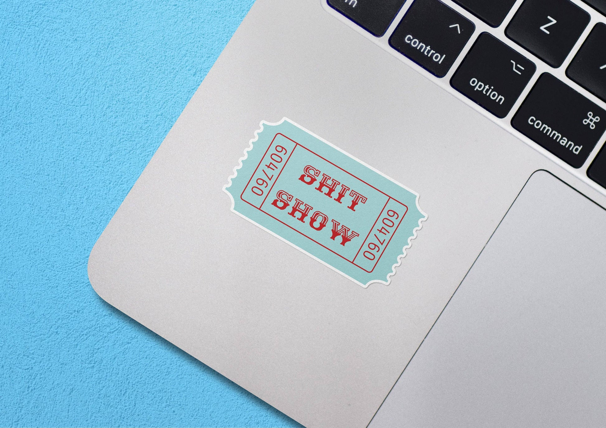 Teal ticket-shaped sticker with SHIT SHOW text on a laptop keyboard.