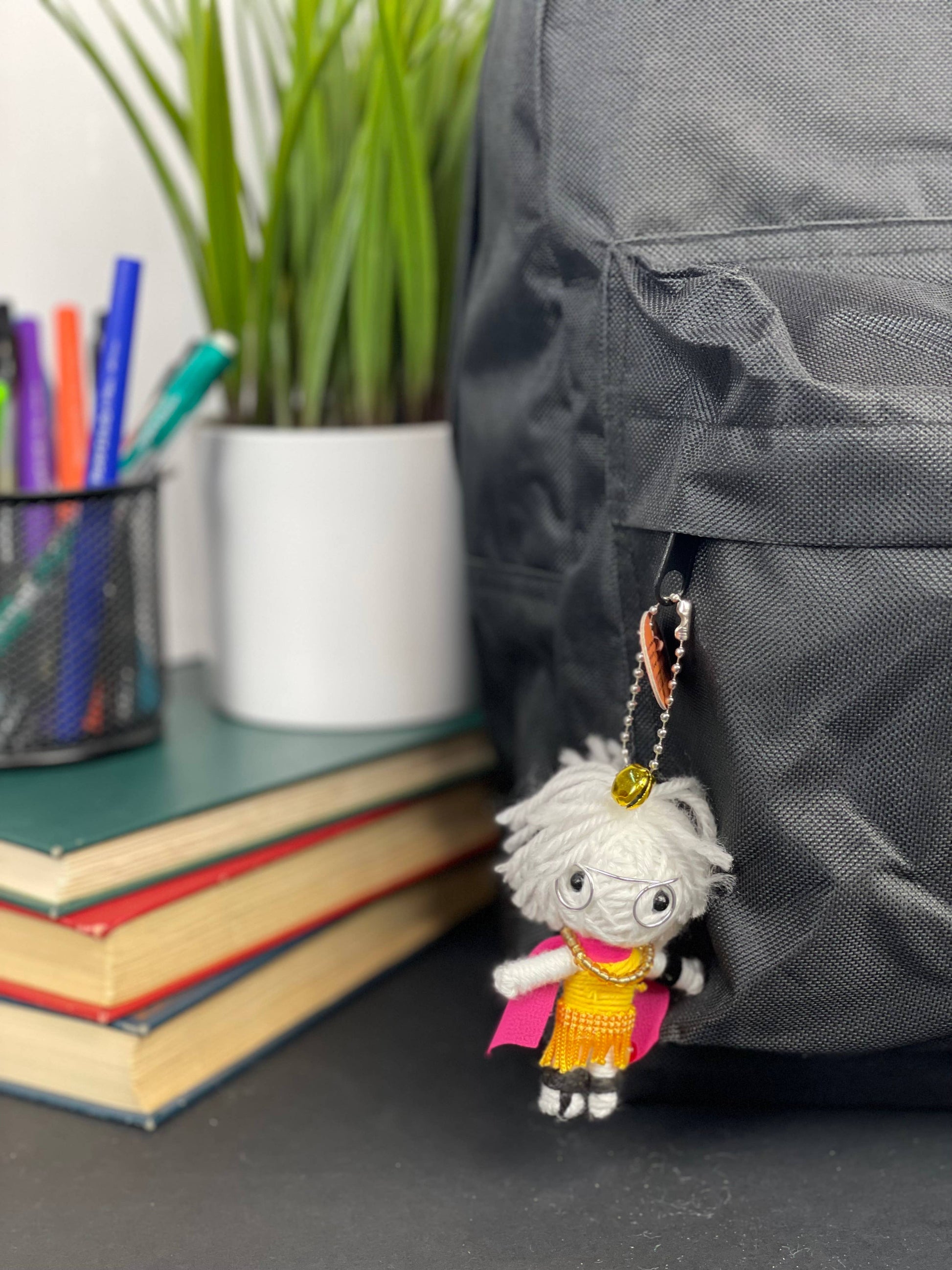 Fuzzy doll charm with glasses and colorful outfit hanging from backpack.