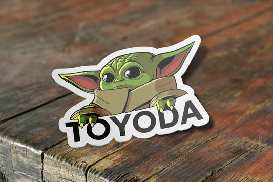 Baby Yoda sticker with TOYODA text on a wooden surface.