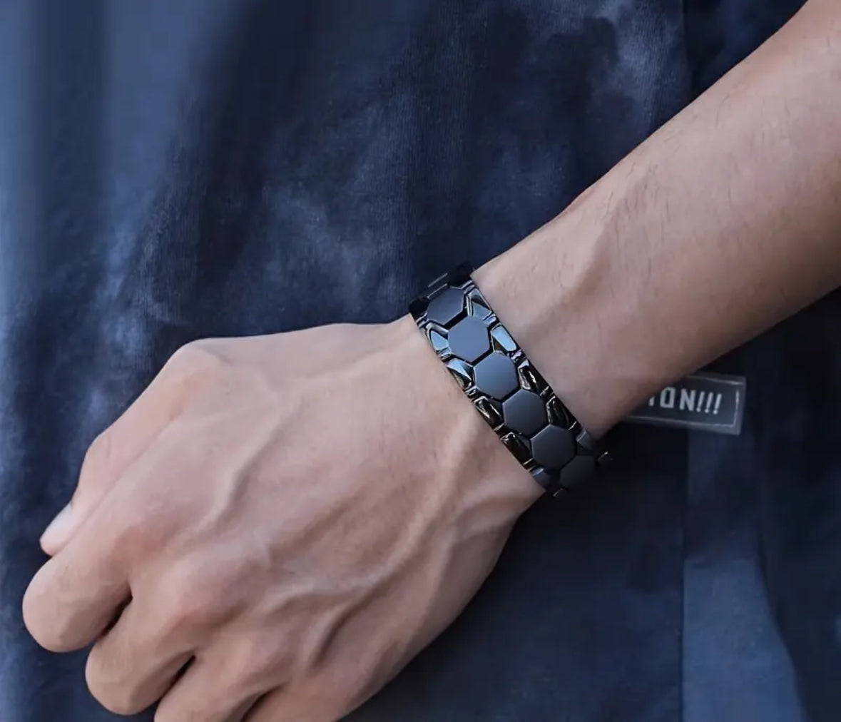 Man wearing black hexagonal patterned bracelet on wrist.