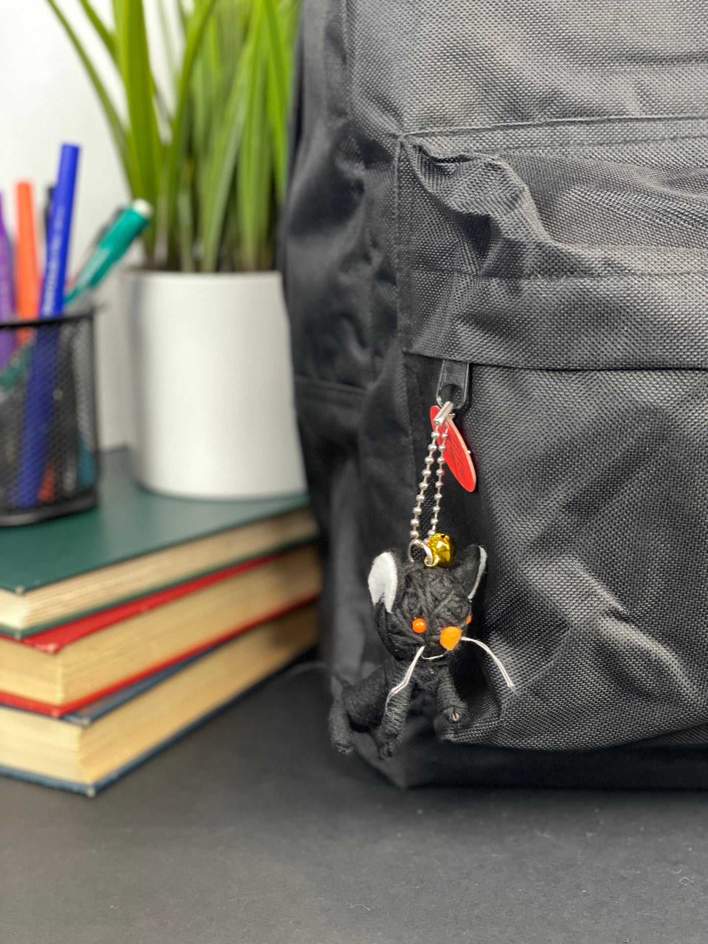 Black backpack with cat-shaped zipper pull and stationery in background.