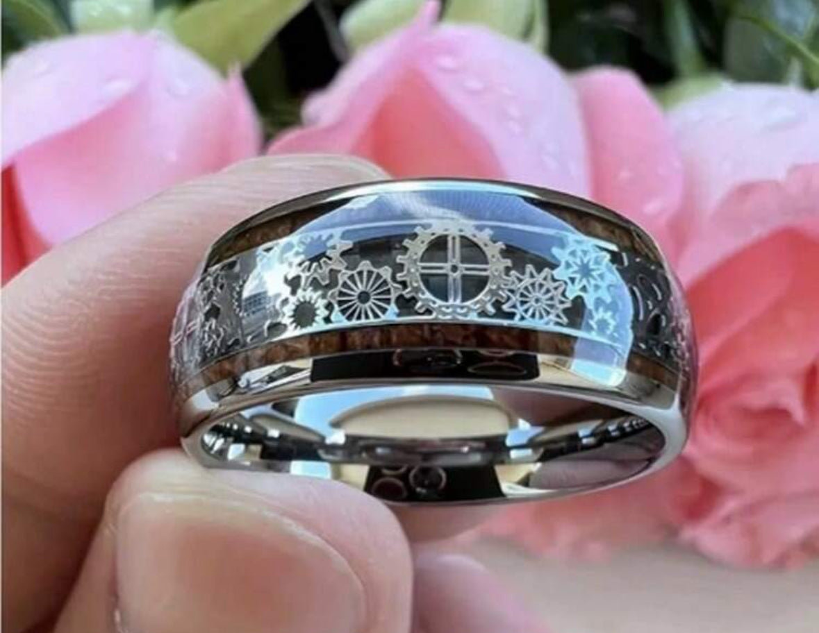 Silver ring with intricate gear design, held against pink flowers.