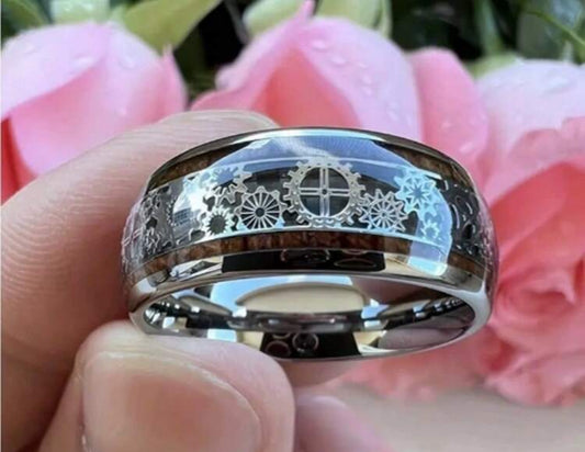 Silver ring with intricate gear design, held against pink flowers.