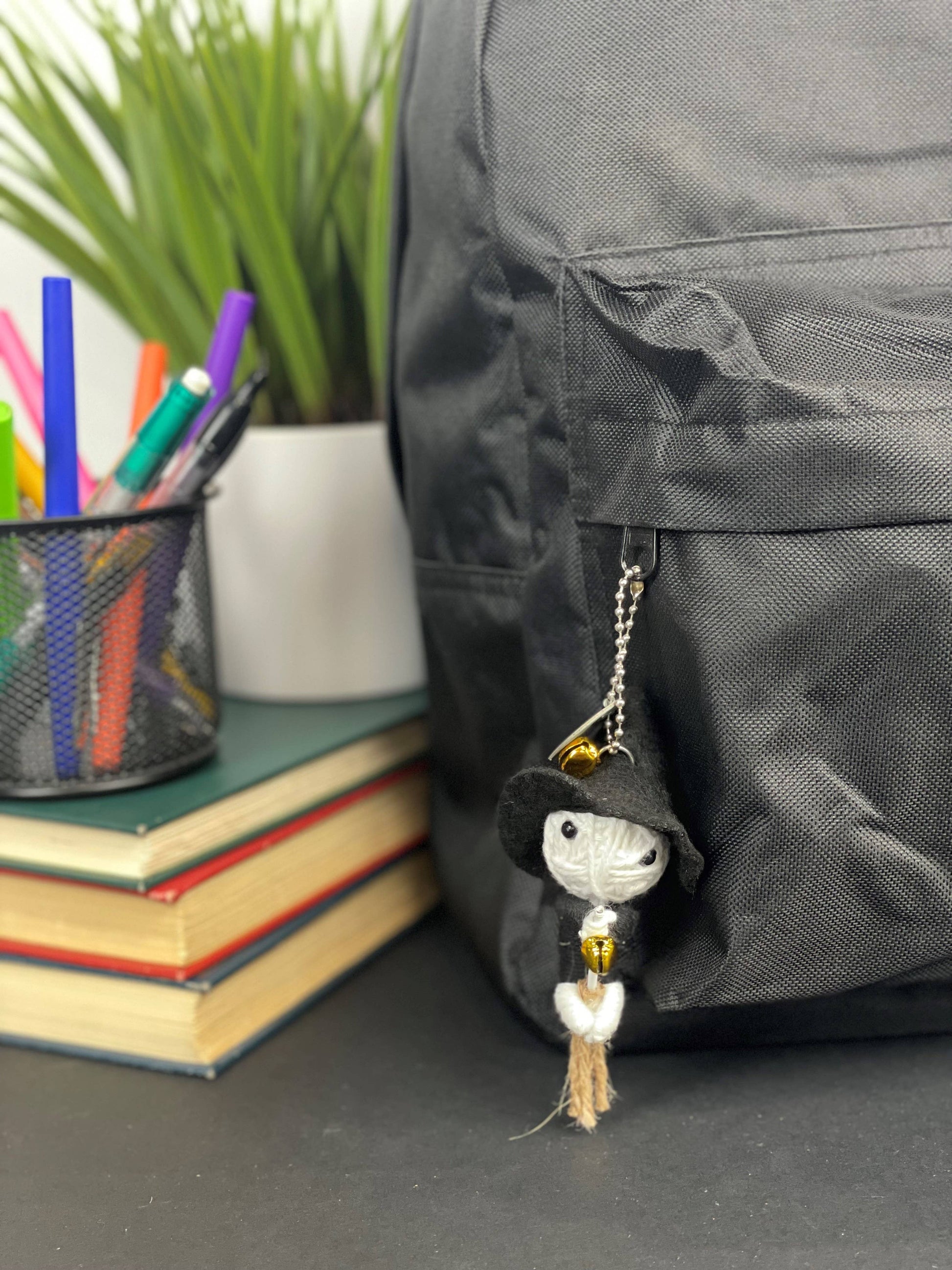 Black backpack with white ghost charm hanging from zipper.