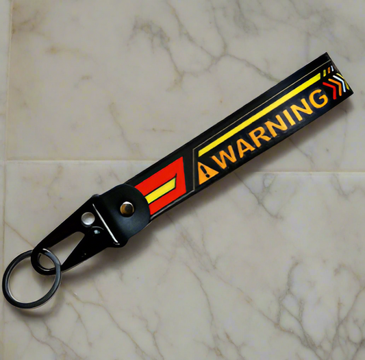 Black keychain with WARNING text and colorful stripes on marble surface.