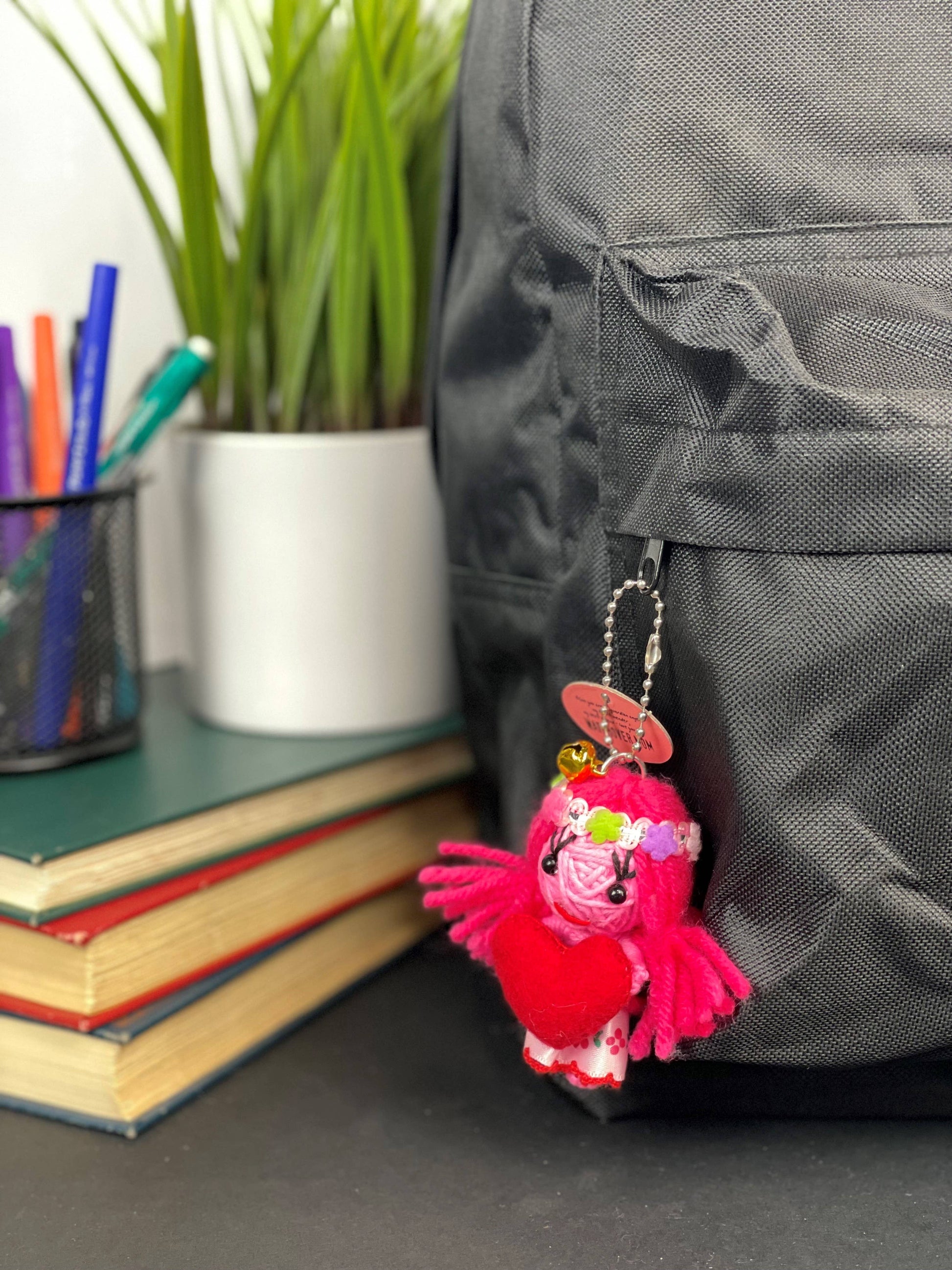 Pink yarn ball charm with heart and beads, hanging from backpack.
