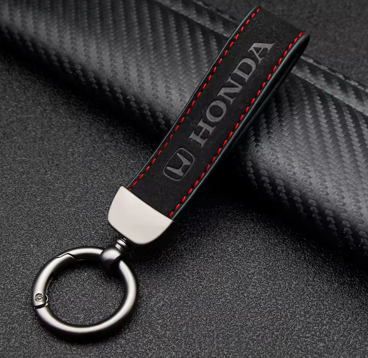 Black Honda keychain with red stitching on a textured surface.