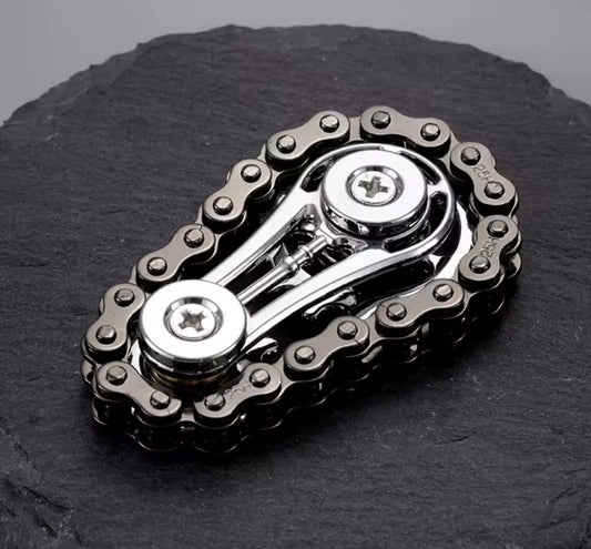 Metal bicycle chain design fidget spinner on black stone surface.