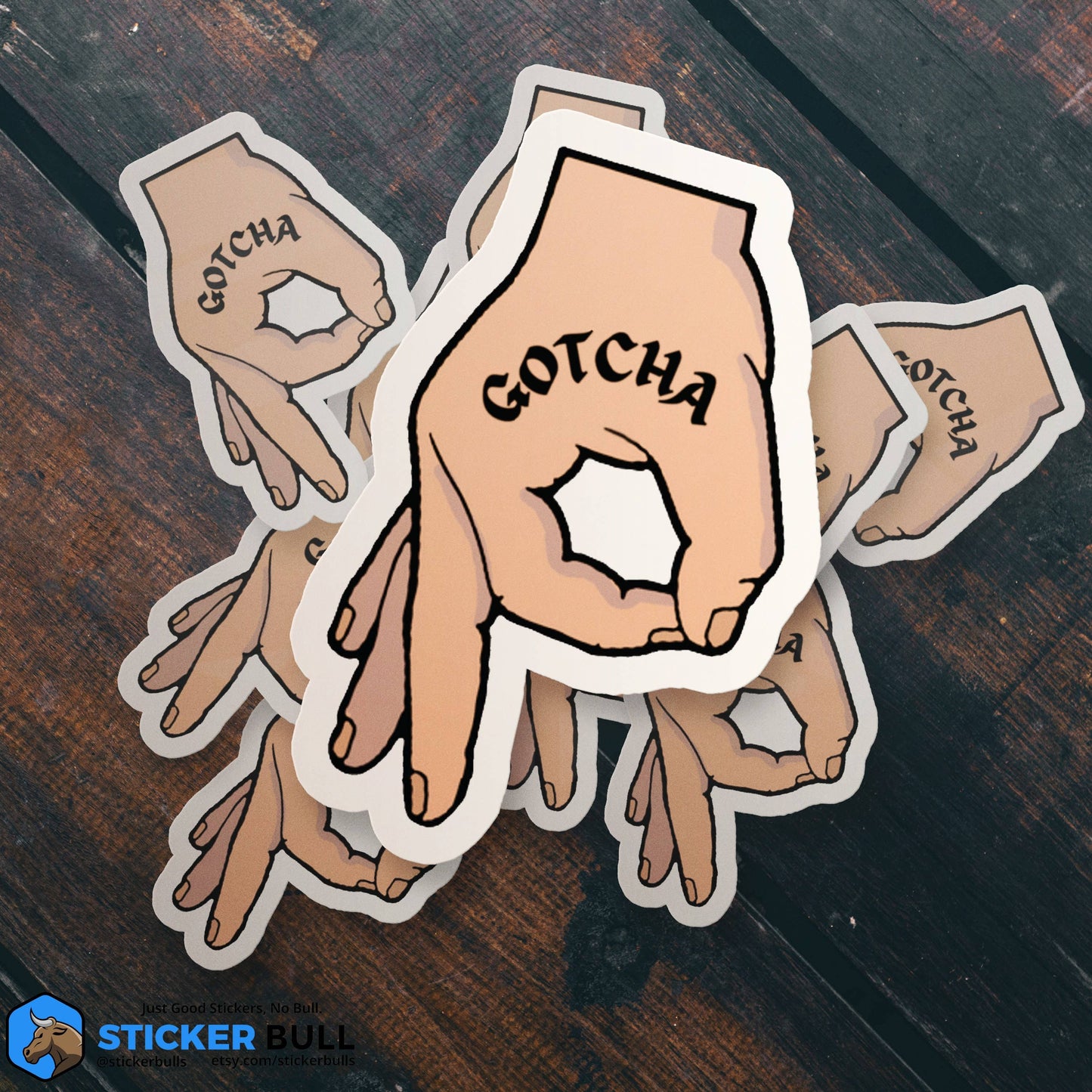 Hand with GOTCHA text sticker design on wooden surface.