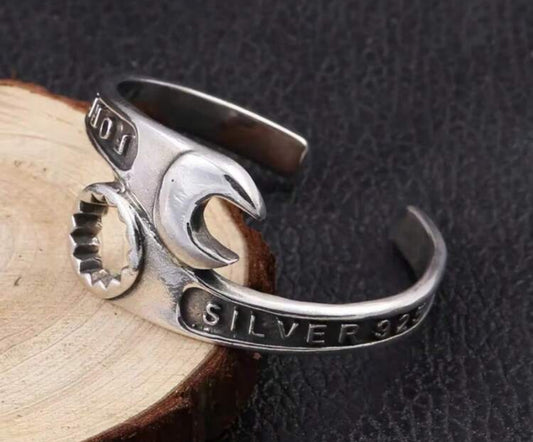 Silver 925 wrench design adjustable ring on wooden surface.