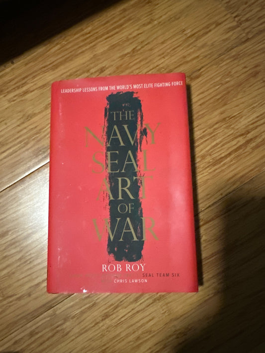Red book titled The Navy SEAL Art of War by Rob Roy on wooden surface.