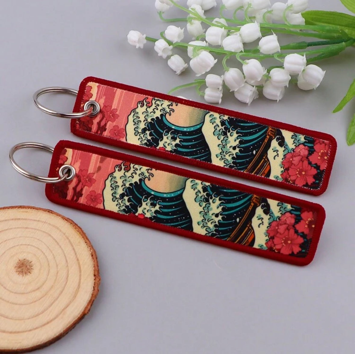 Red keychains with wave and floral design, wooden slice, white flowers.