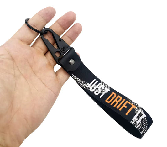 Black keychain with JUST DRIFT text and tire tread design, held in hand.