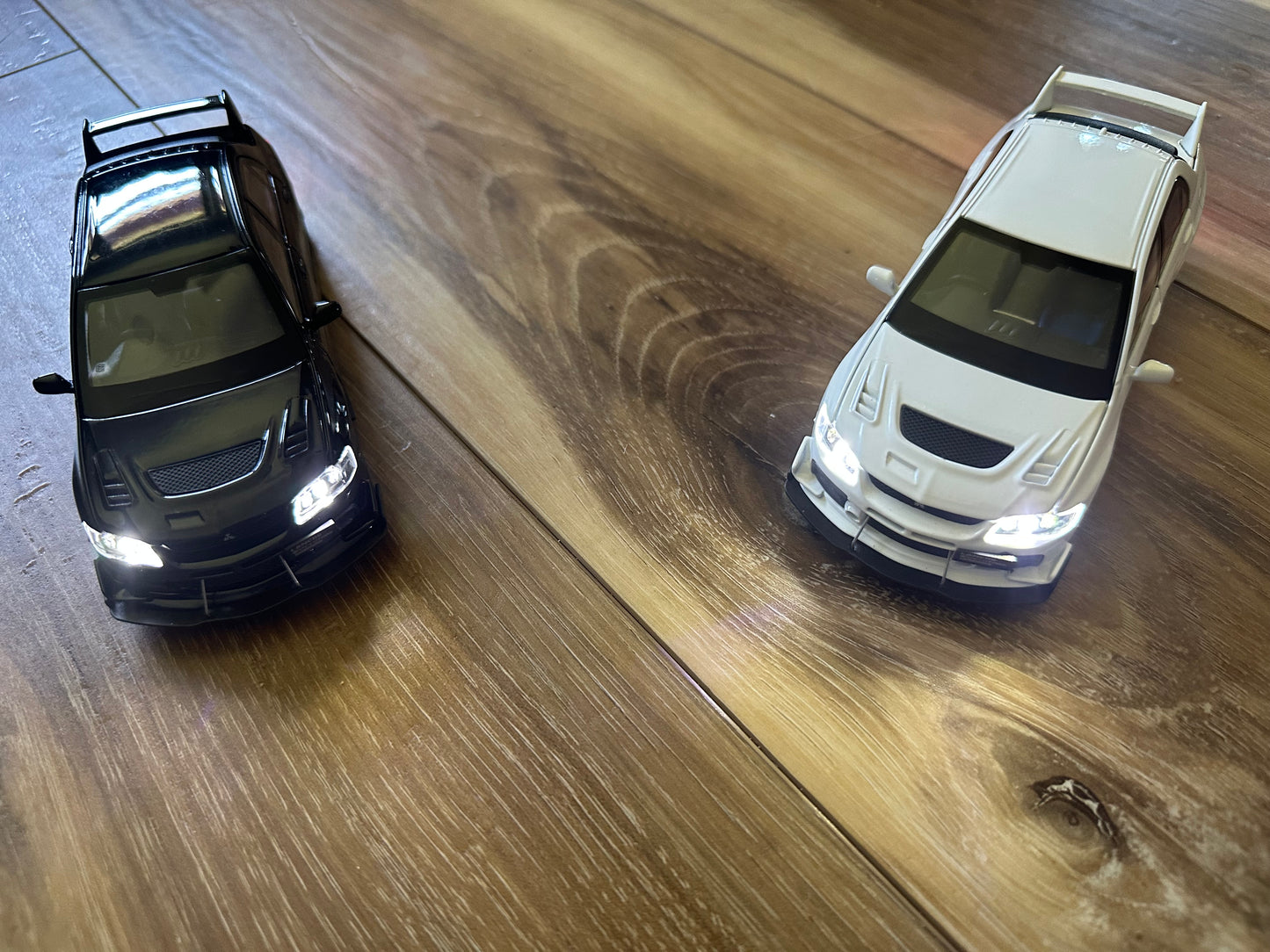 Two toy cars, one black and one white, on a wooden floor.