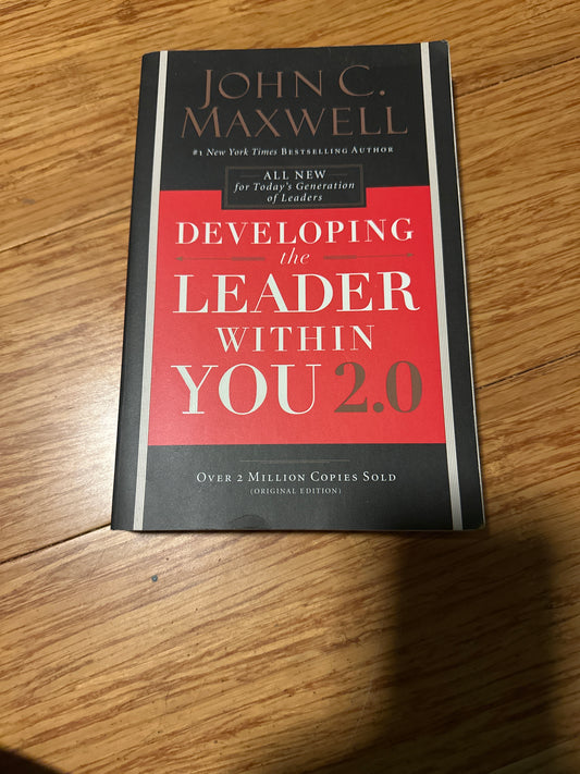 Book cover of Developing the Leader Within You 2.0 by John C. Maxwell on wooden surface.