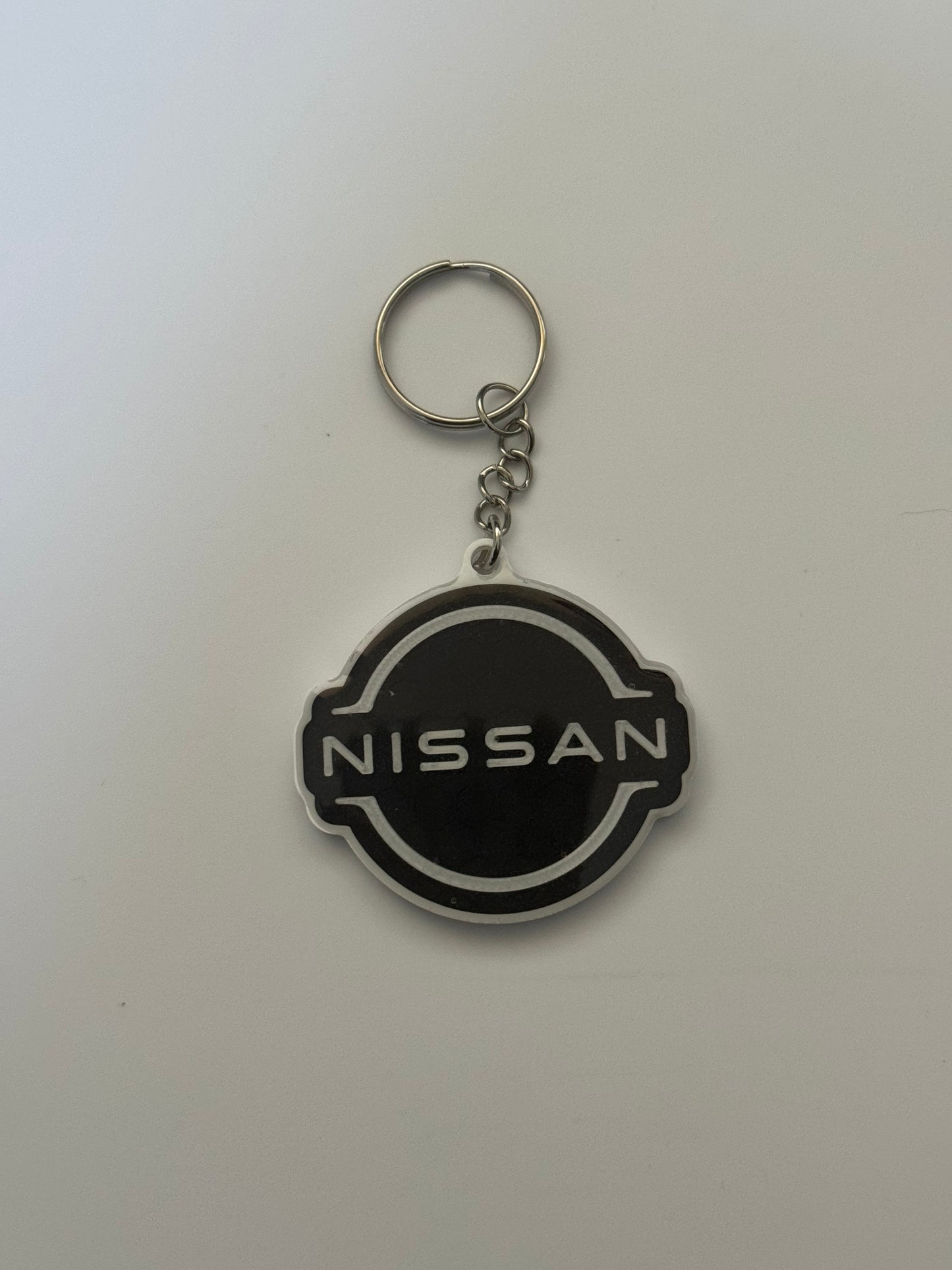 Black and white Nissan logo keychain with silver ring on a plain background.