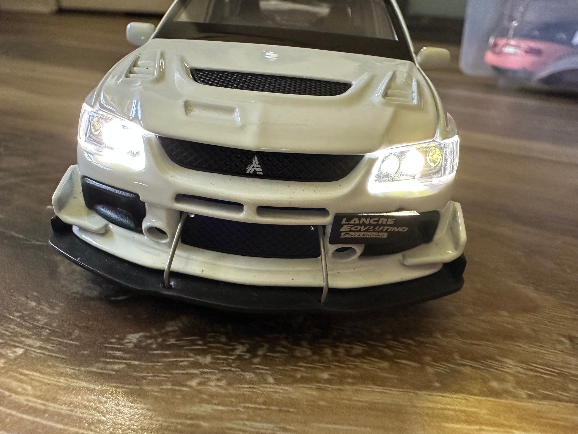 White Mitsubishi Lancer Evolution model car with front bumper and headlights.