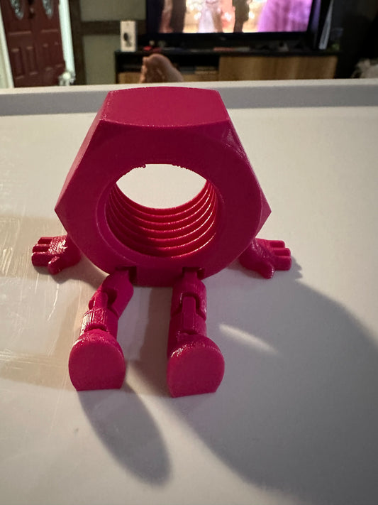 Pink 3D-printed nut with legs on white surface.