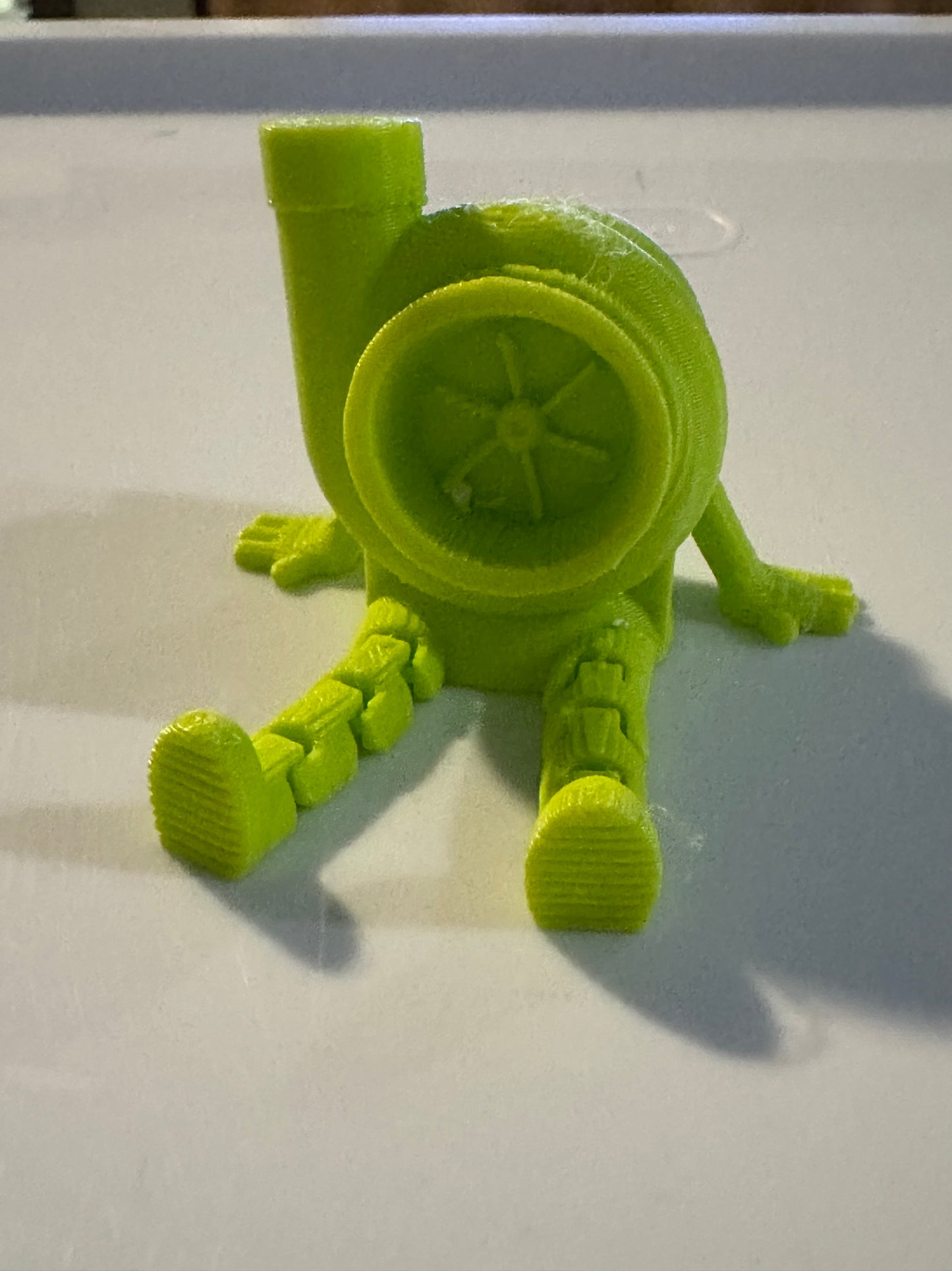 Green 3D-printed toy with circular wheel and four legs on white surface.