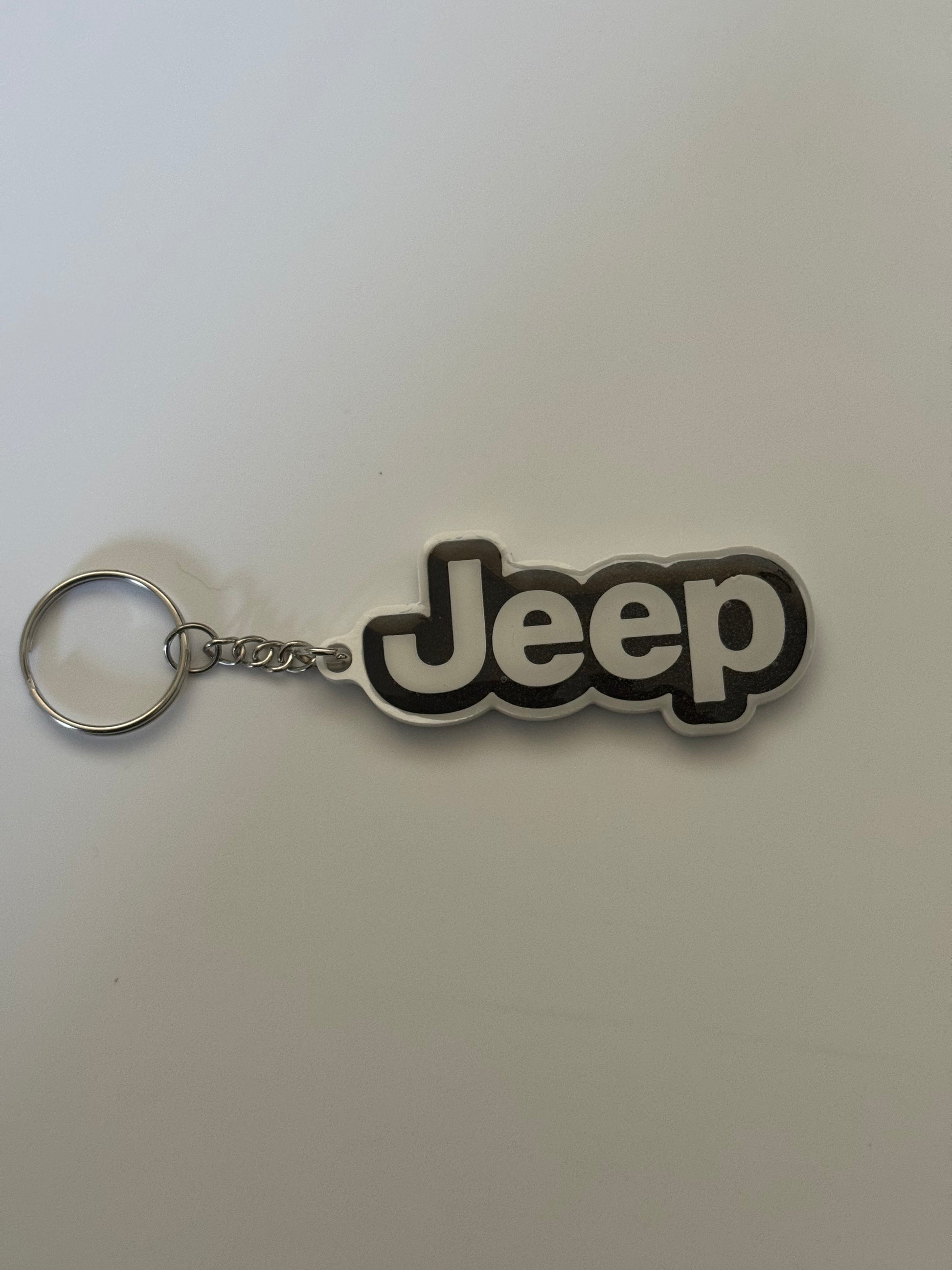 Jeep logo keychain with silver ring and chain on a plain background.